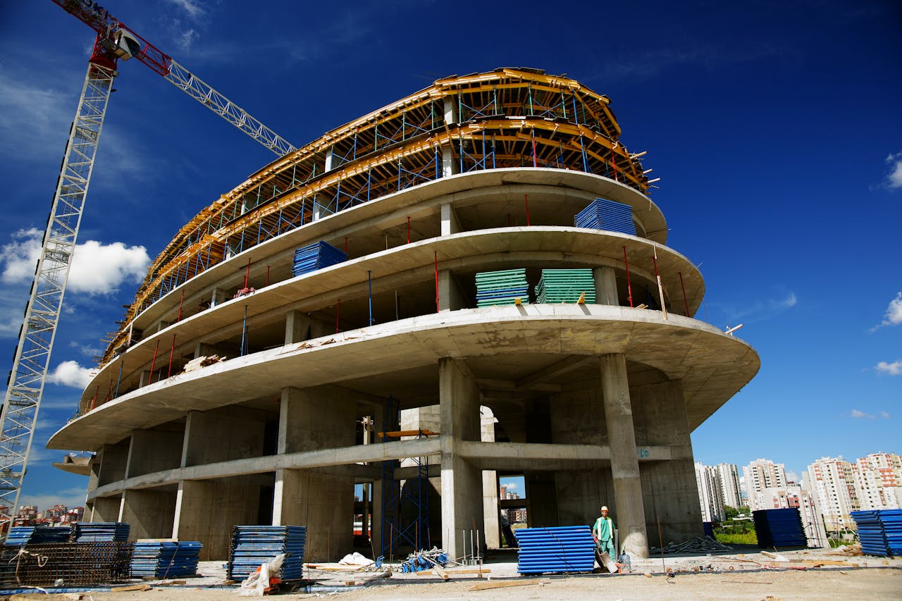 Low angle view of a circular building under construction with a crane, clear blue sky.